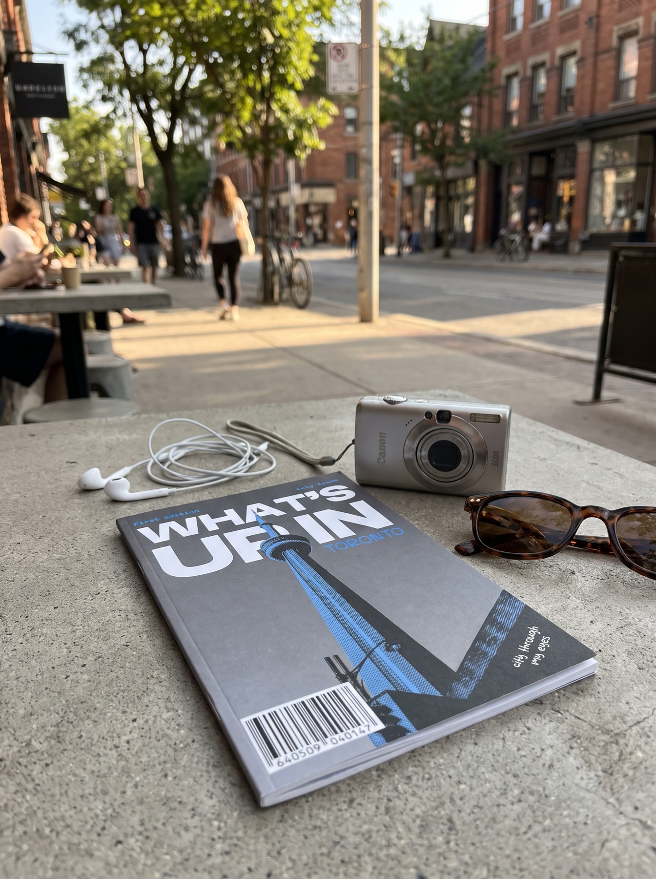 What's Up In Toronto zine, first issue, sitting on a Kensington Market patio table next to a film camera and sunglasses